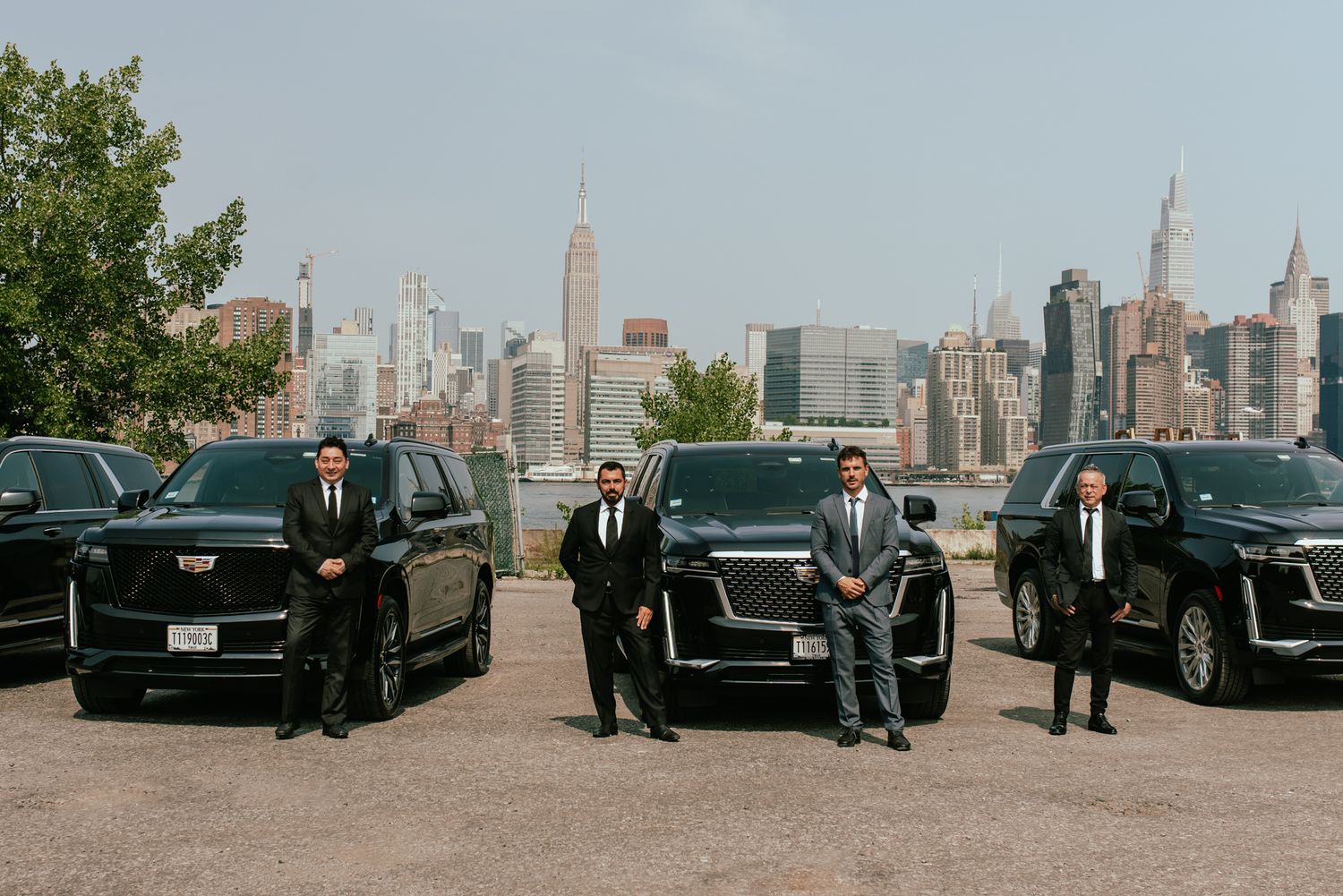 A line of black luxury vehicles parked with the New York City skyline in the background.