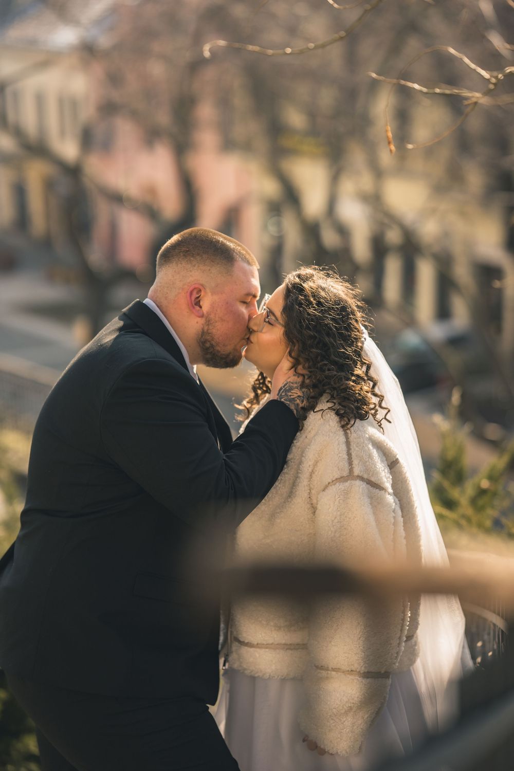 Intimate winter wedding portrait of couple kissing with bare branches in background.