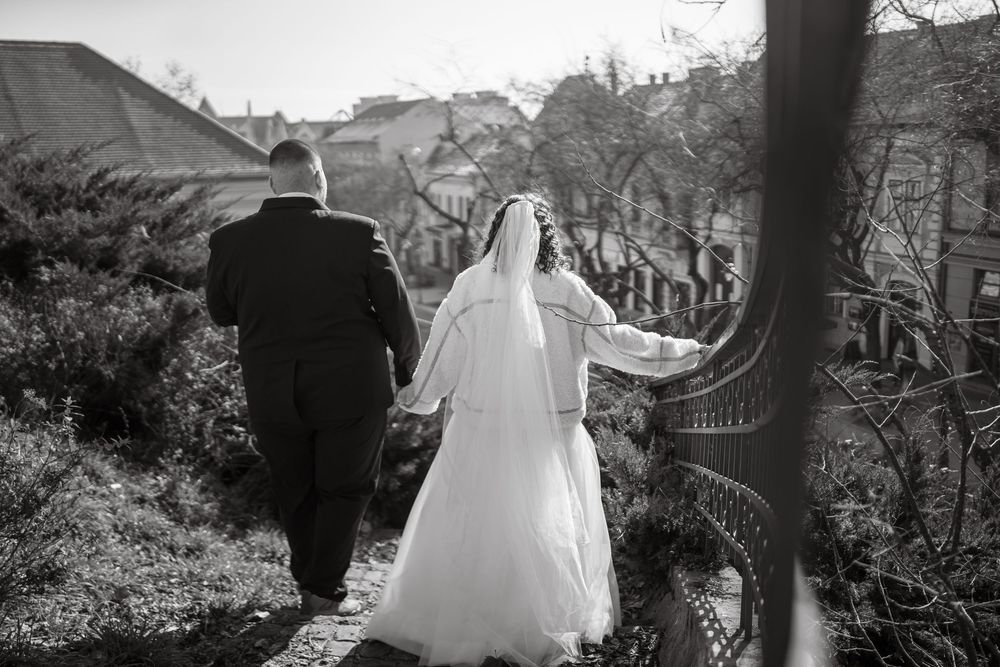 A black and white wedding photo showing a couple walking away on a tree-lined path in their formal attire.