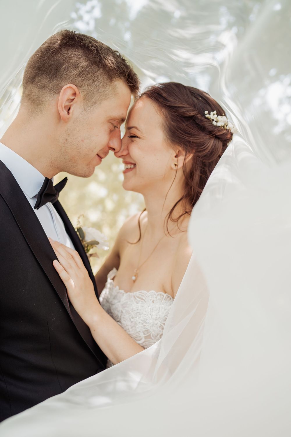 Romantic close-up wedding portrait of newlywed couple about to kiss against bright bokeh background.