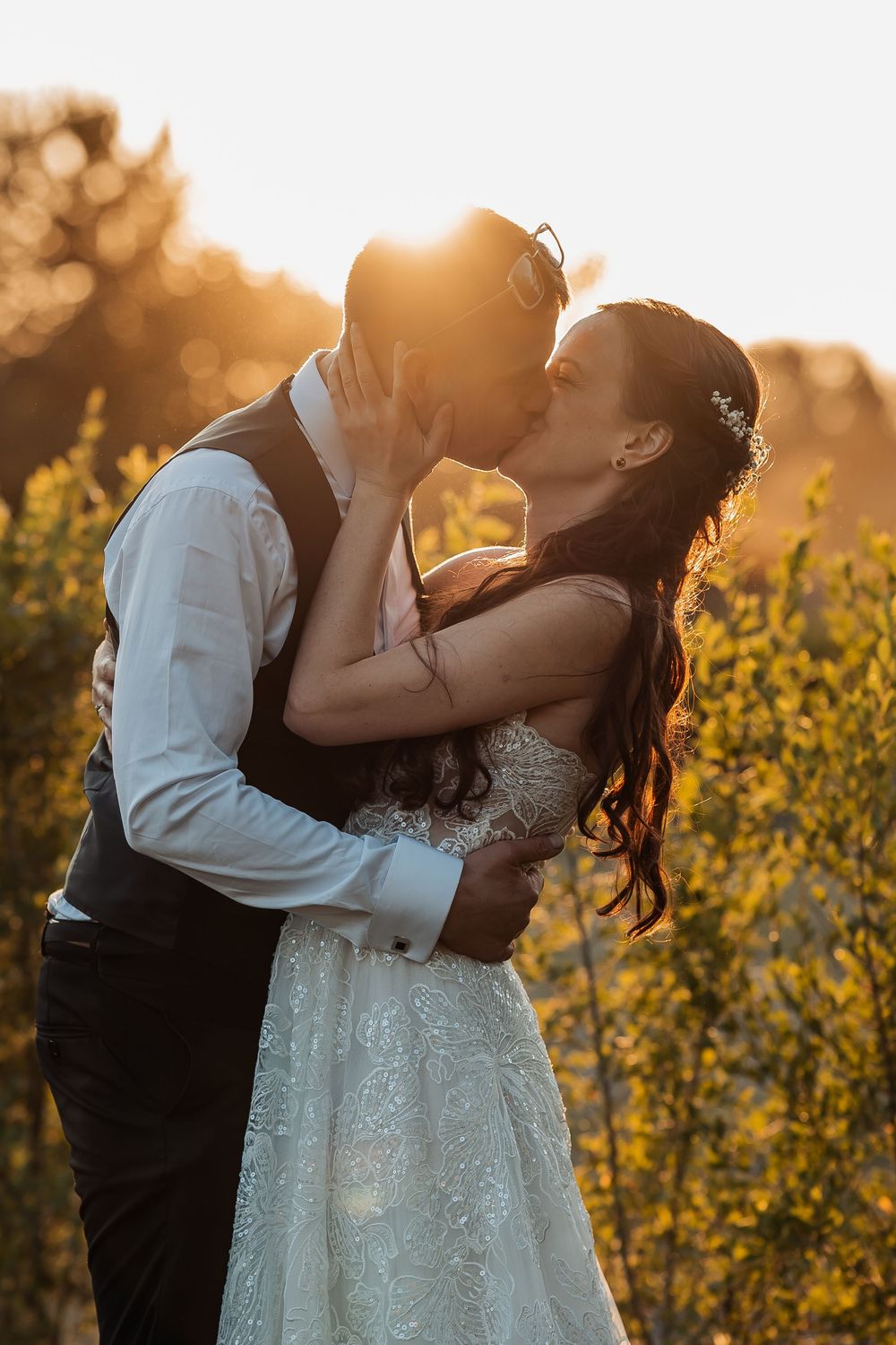 Newlyweds share a passionate kiss during golden hour in a field of wildflowers.