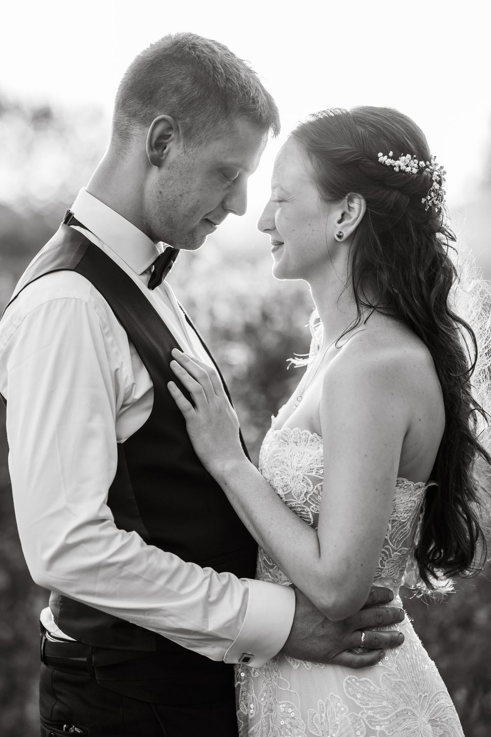 A tender black and white wedding photograph showing a romantic moment between newlyweds in formal attire.