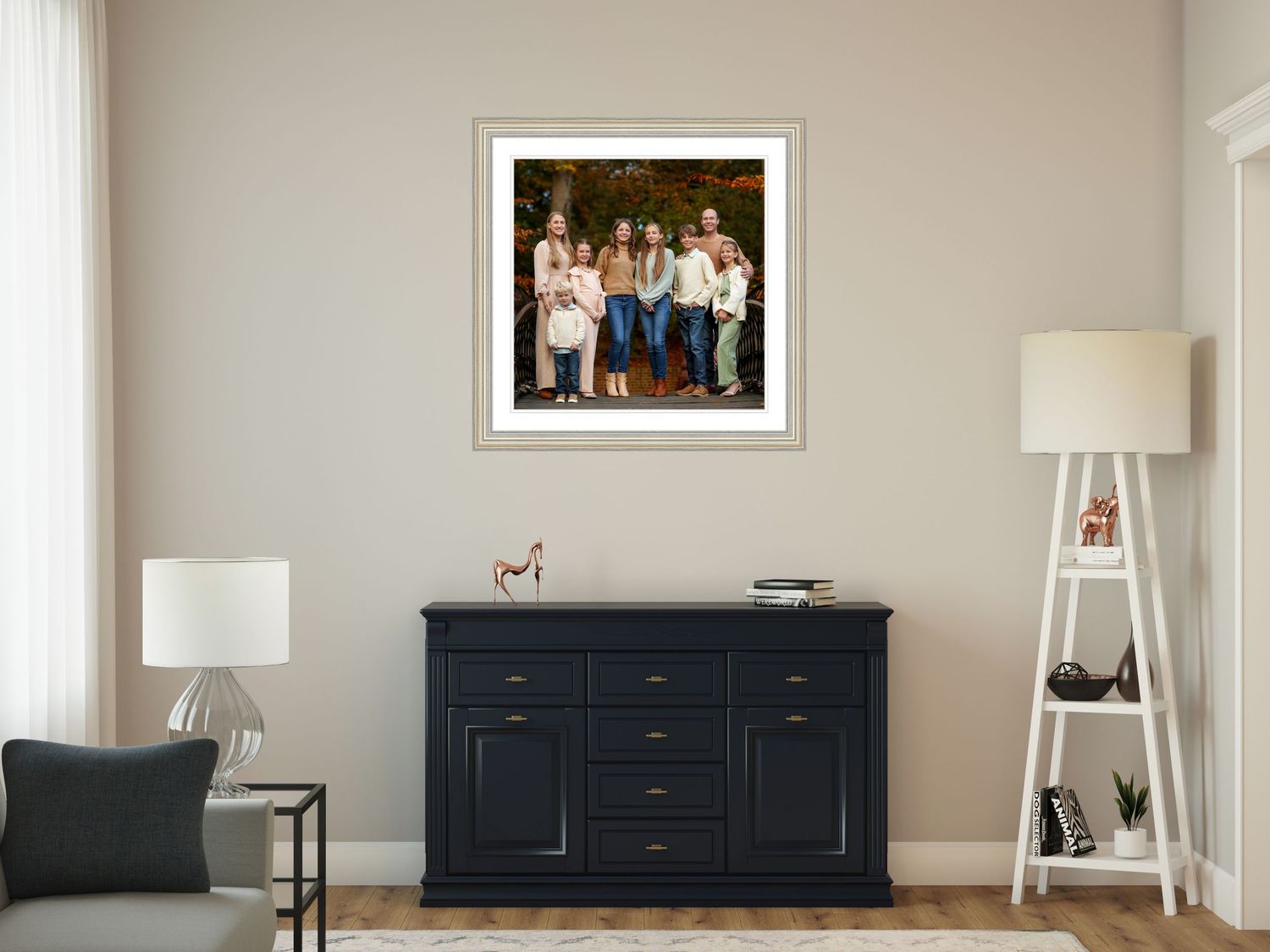 A black wooden sideboard cabinet sits beneath a framed family portrait, with white lamps and a ladder shelf in a modern room.