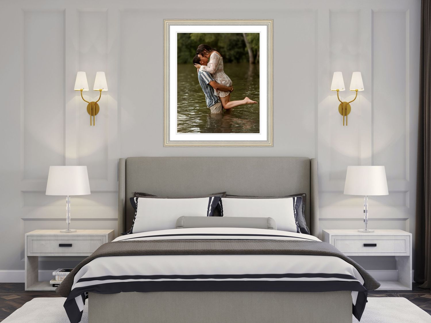Contemporary bedroom interior with gray upholstered bed, white nightstands, wall sconces and framed artwork above headboard.