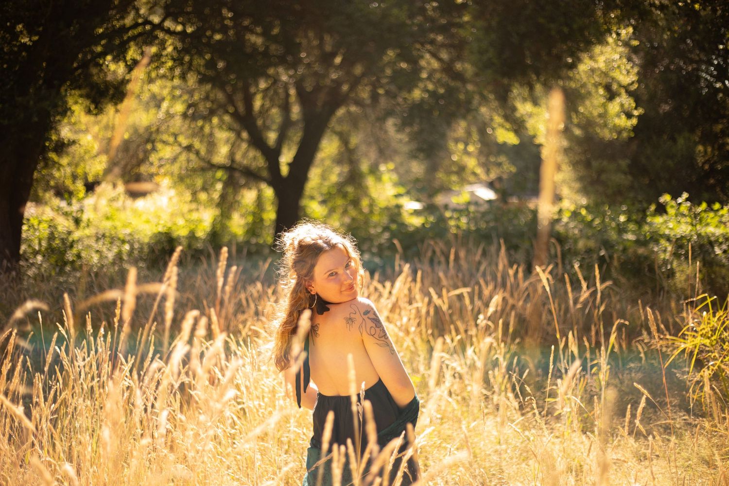 Sunlit silhouette of a person with long hair standing in golden grass during golden hour surrounded by dreamy light.