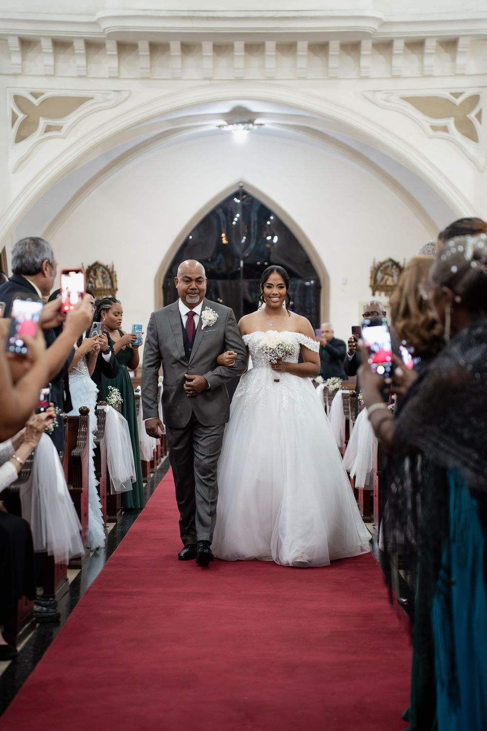 Wedding attendees line a red carpet aisle while taking photos as the couple walks down for their grand exit.