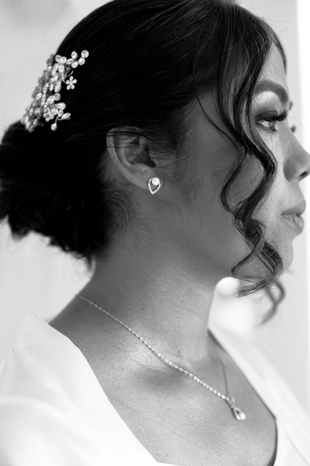 Black and white profile shot of a bride wearing delicate jewelry and a floral hair accessory.