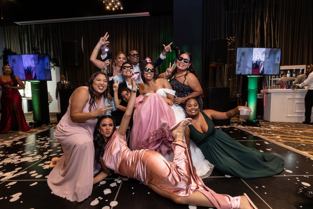 Wedding party celebrates on dance floor with pink bridesmaid dresses and confetti at evening reception.