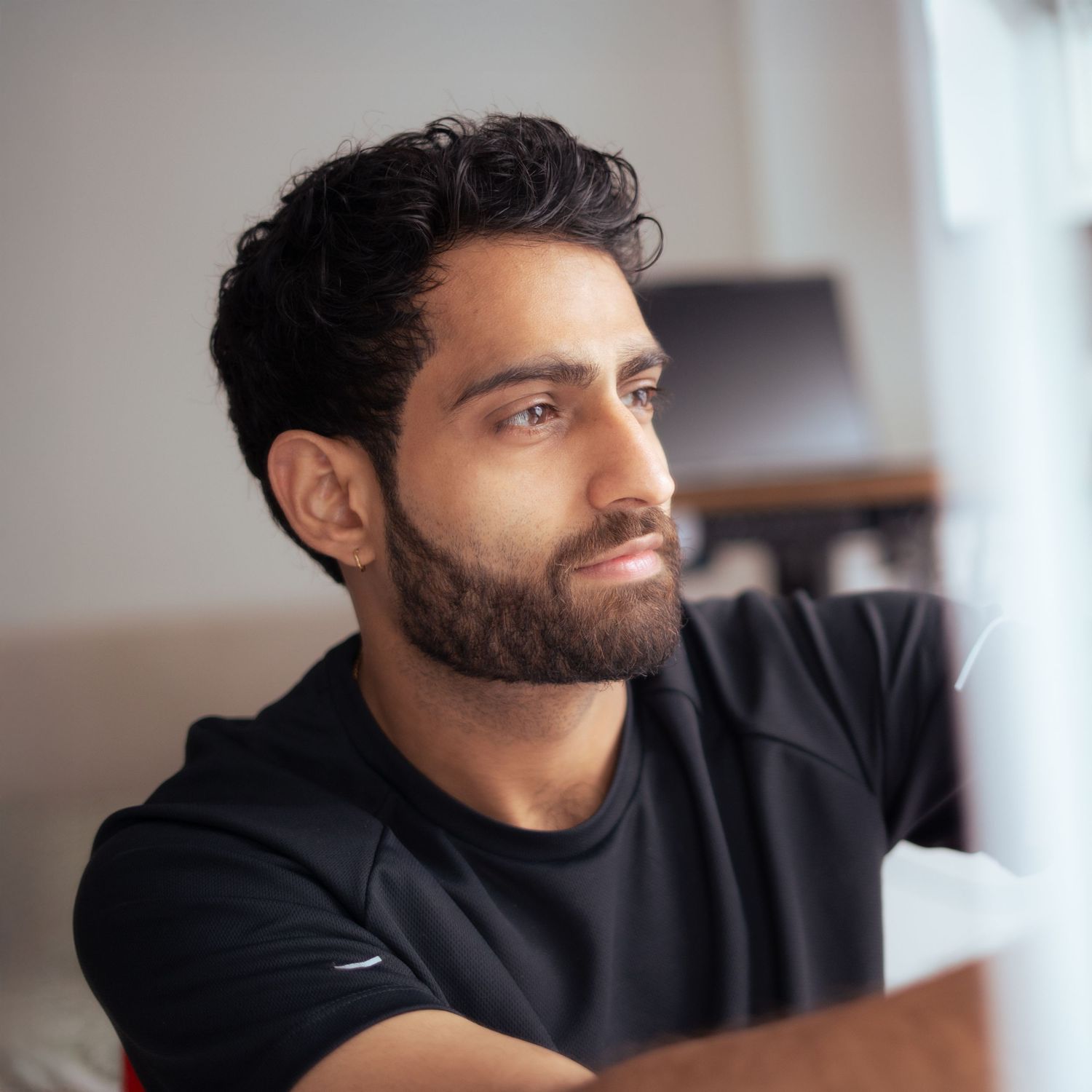 Side profile portrait of person with dark beard and curly hair wearing black shirt looking thoughtfully to the side.