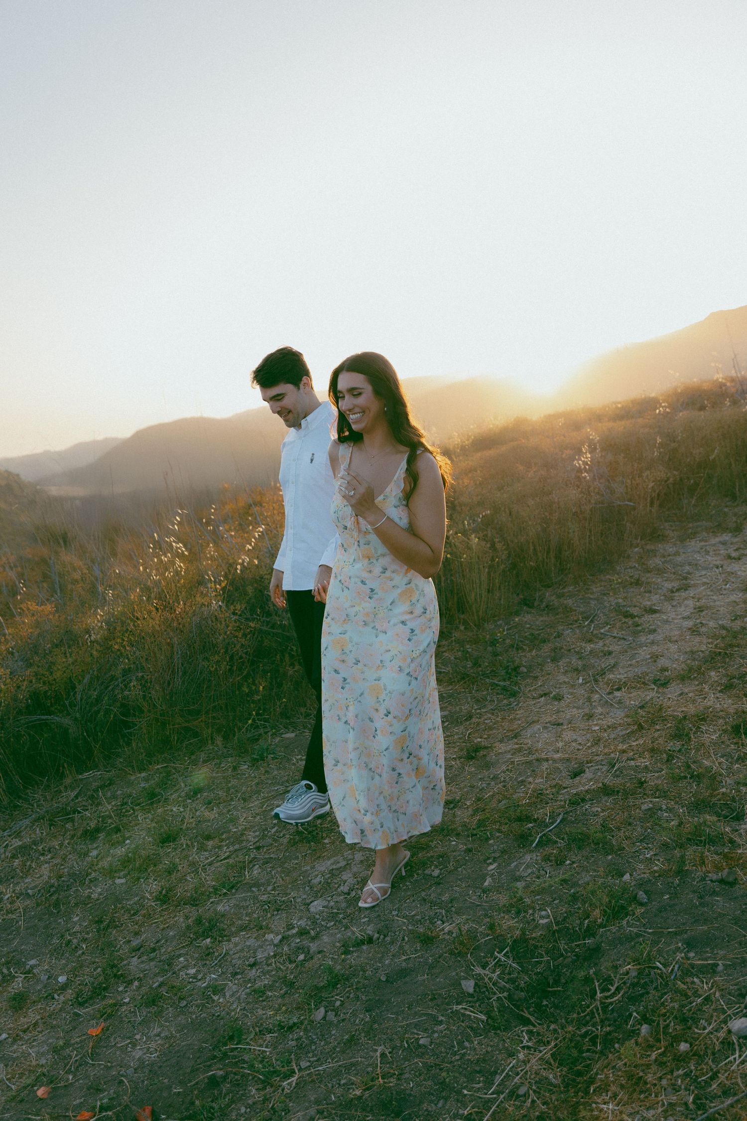 A couple shares a tender embrace while standing on a hillside trail during golden hour sunset.