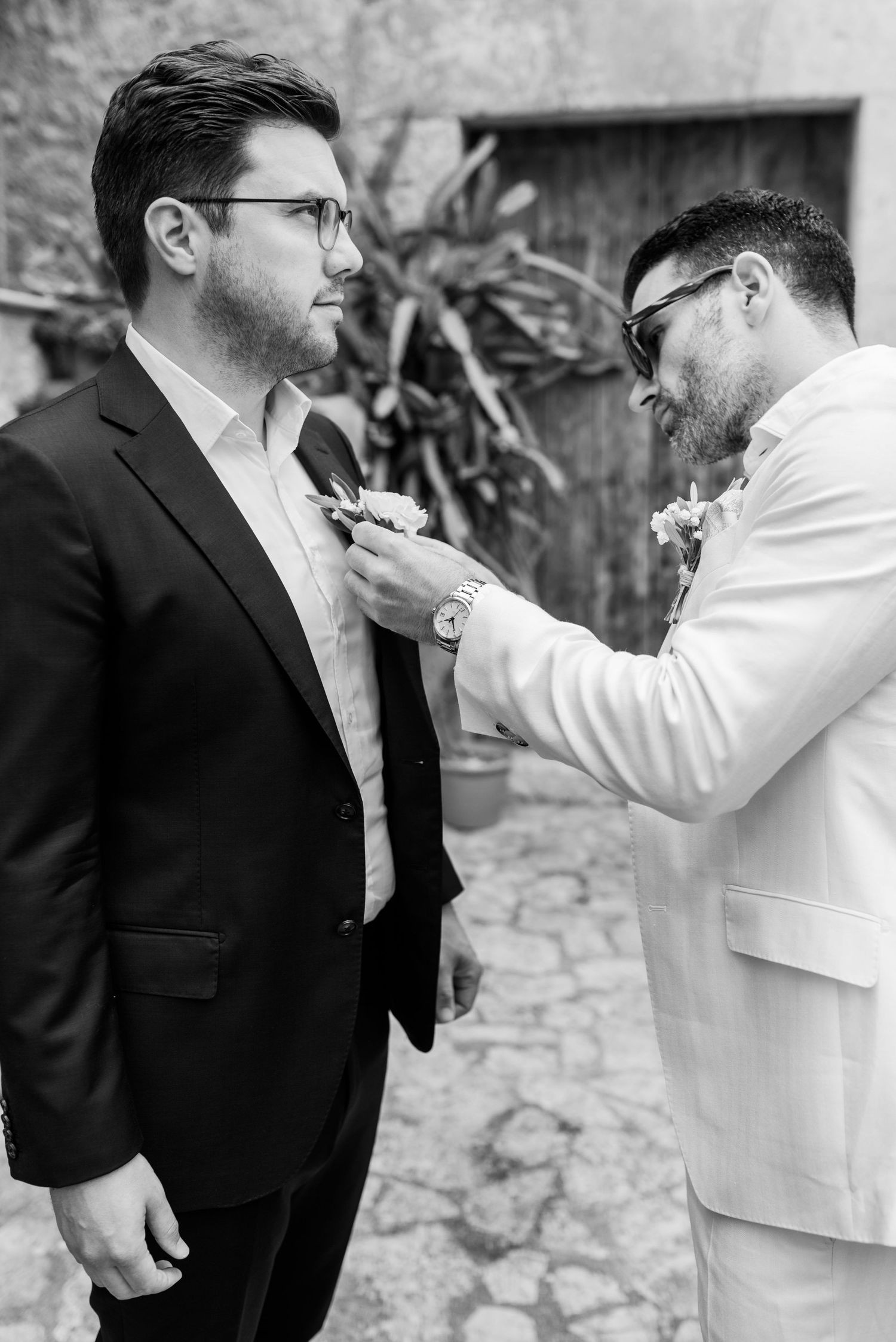 Beim Getting Ready teilen sie einen ehrlichen Schwarz-Weiß-Moment, während der Bräutigam dem Trauzeugen die Ansteckblume ansteckt. Finca