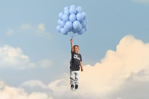 A person holding a cluster of light blue balloons against a bright cloudy sky, suggesting freedom and serenity.