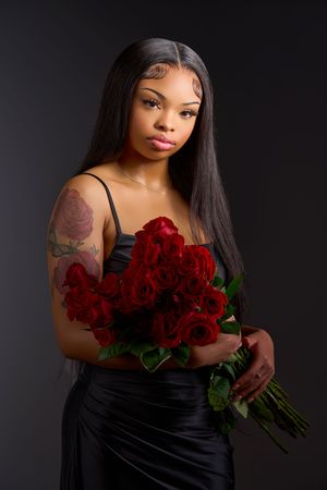 A glamorous photoshoot featuring a dramatic black dress and deep red roses against a dark studio backdrop.