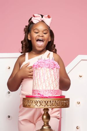 Joyful expressions and pink birthday cake on gold stand against pink backdrop create celebratory photo series.