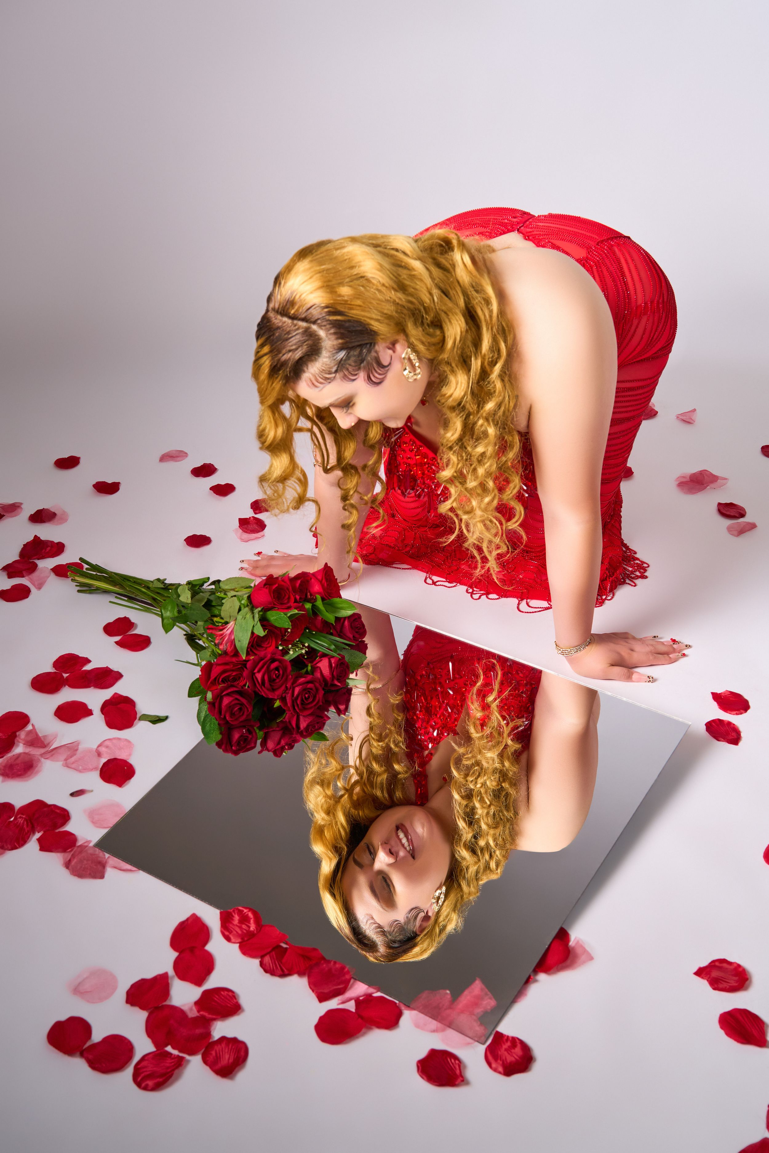 Elegant fashion shoot with red roses and scattered petals against white backdrop.
