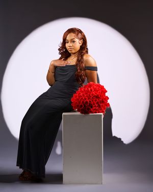 Elegant studio portrait featuring black evening gown and bright red carnation bouquet against white circular backdrop.