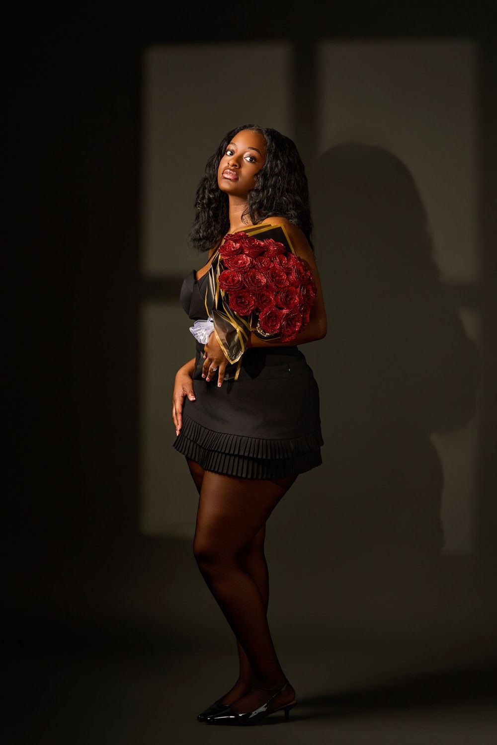 Dynamic fashion photoshoot featuring figure in black outfit holding vibrant red roses against dark background.