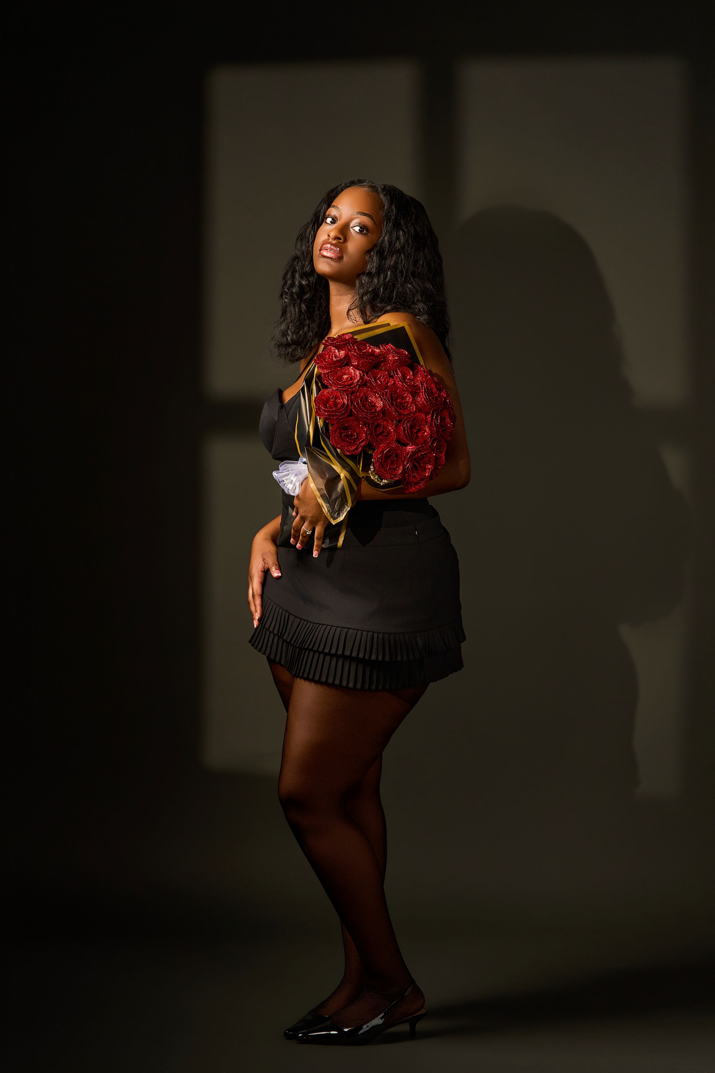 Dynamic fashion photoshoot featuring figure in black outfit holding vibrant red roses against dark background.