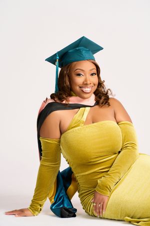 Graduate in teal cap and yellow off-shoulder dress poses gracefully during a photo session.