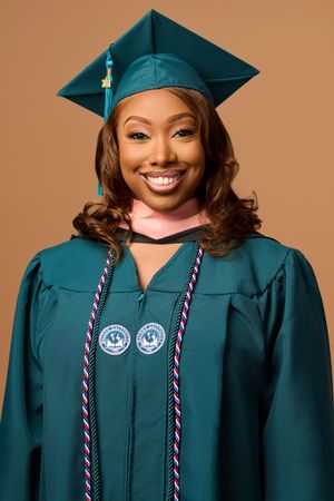 Graduate wearing emerald green academic regalia with honor cords and medallions against a tan background.