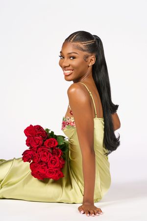 Elegant photo of a model in a lime green satin dress holding vibrant red roses against a white backdrop.