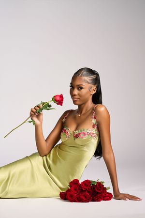 A woman in a lime green silk dress poses elegantly with red roses against a light gray studio background.