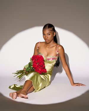 Model in satin lime dress poses elegantly with red roses against neutral backdrop in artistic fashion series.