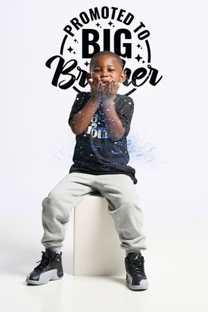 A young child in casual wear sits on a white stool with text 'Promoted to Big Brother' overlaid on the photo.