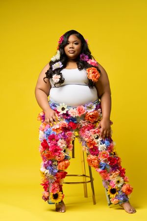 Person in white top and floral pants poses against vibrant yellow backdrop in artistic fashion photoshoot.