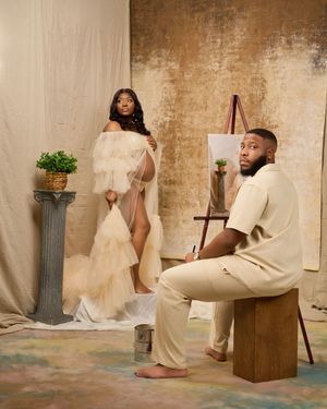 An artistic maternity photo shoot in a studio with cream tones featuring a couple posing against a textured wall.