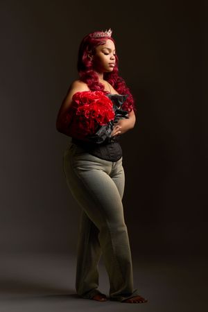 Glamorous portrait featuring vibrant red hair and matching red roses against dramatic dark lighting in a studio setting.