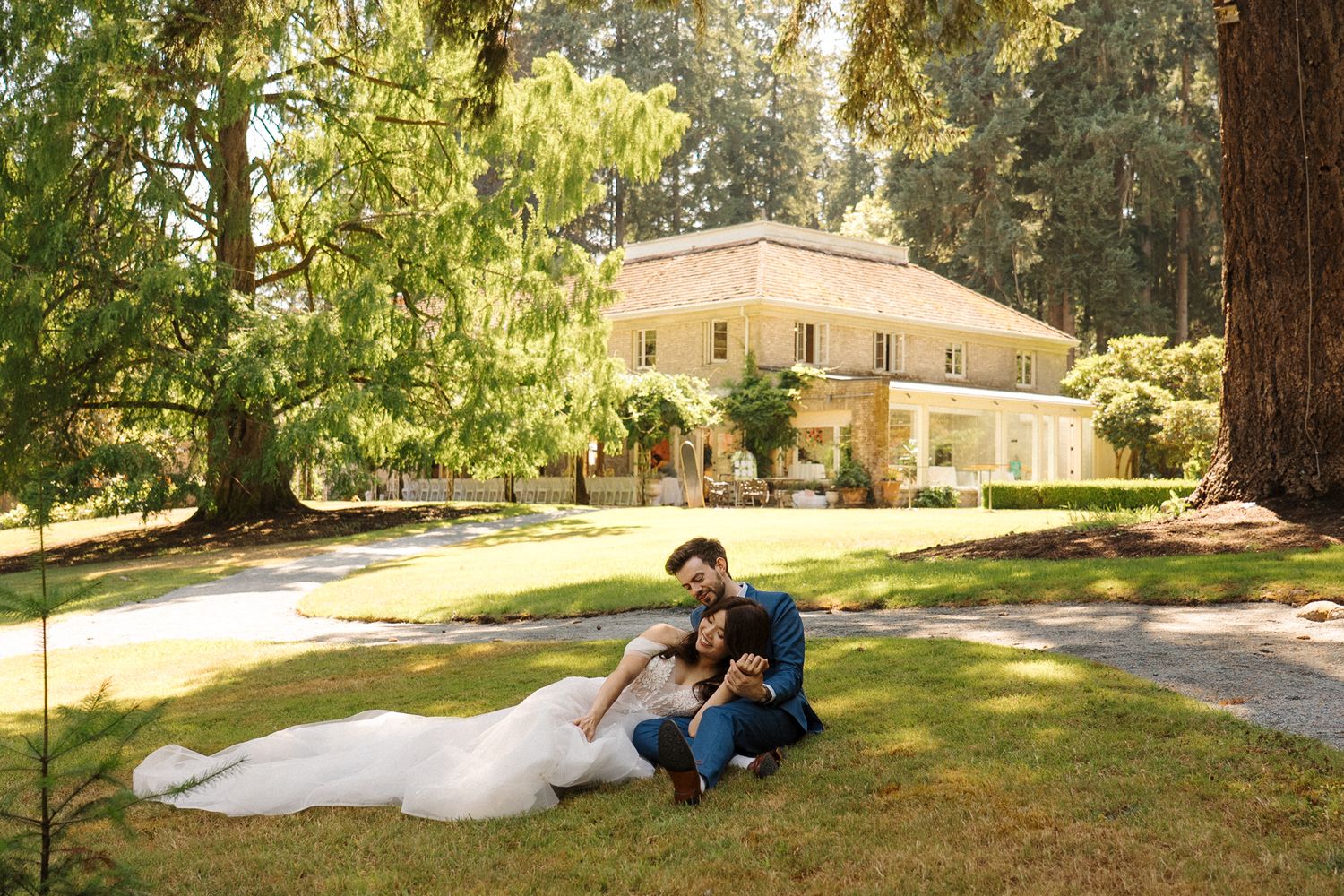 A person and their pet dog sit together on a scenic trail beneath tall evergreen trees in a peaceful forest setting.