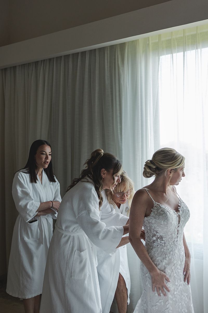 Bridesmaids helping bride into dress at Fairmont Mayakoba Riviera Maya wedding photographer.