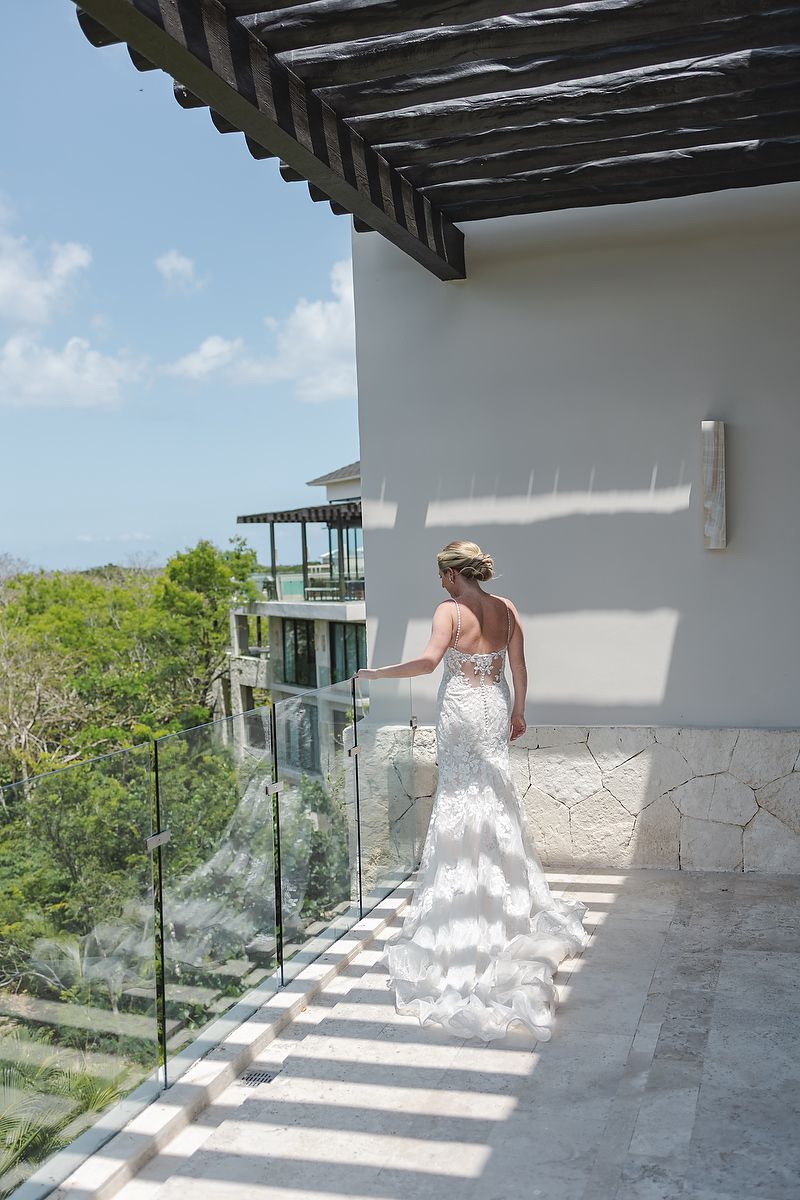 Someone in a white lace wedding dress stands on a balcony overlooking tropical scenery at a luxury resort.