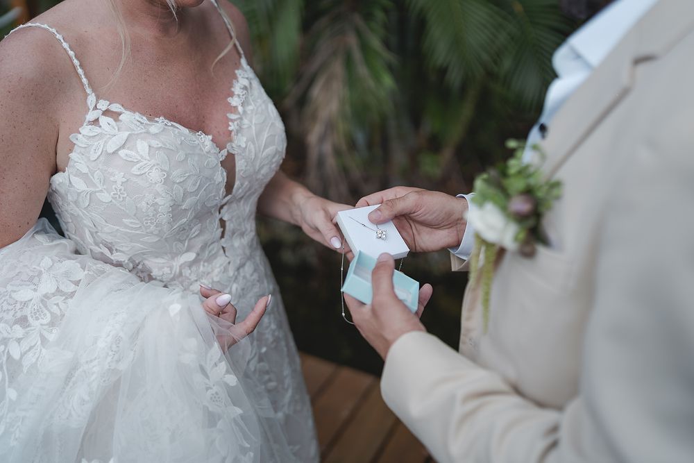 Close up view of hands exchanging wedding rings during an intimate ceremony with bride wearing lace gown.