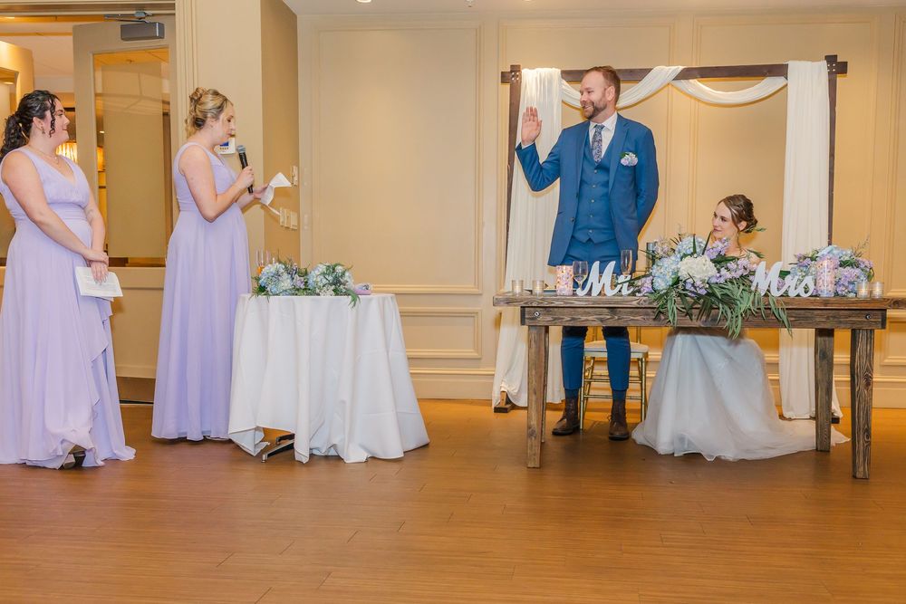 Celebration scene at a wedding reception with bridesmaids in lavender dresses and a groom in blue suit toasting.