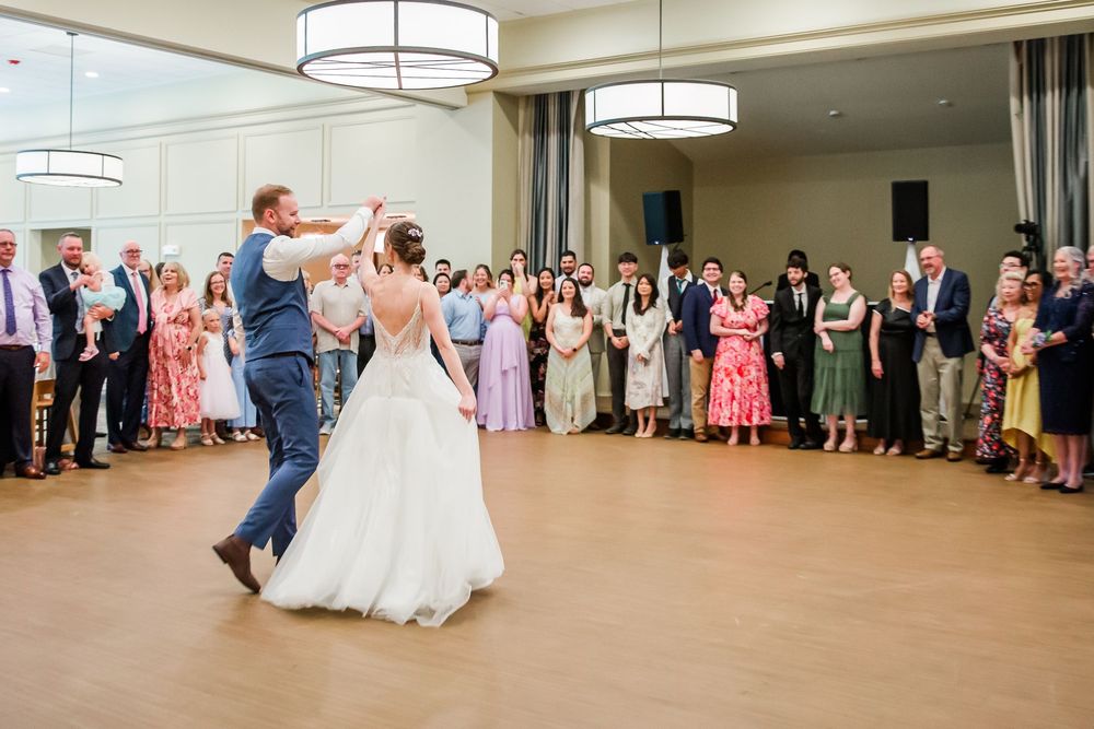 Wedding guests gather around the dance floor as a couple dances at an elegant indoor reception venue with drum pendant lights.
