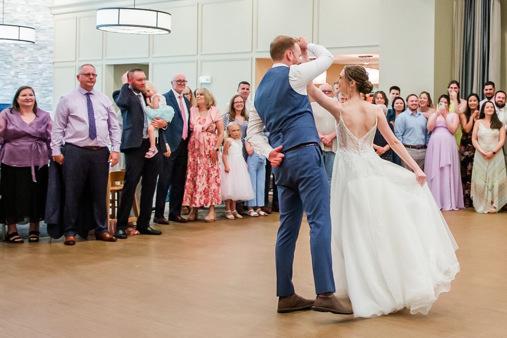 A couple in wedding attire dances in the center of a reception hall while guests watch from the sidelines.