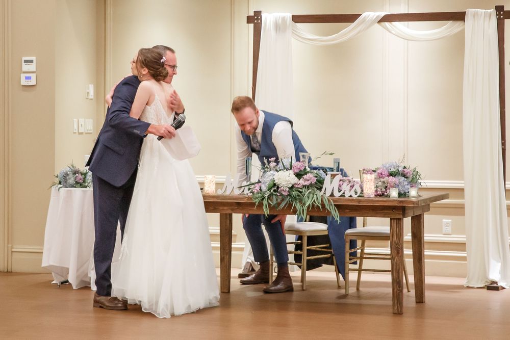 An elegant reception hall decorated with a wooden table and cross wall decor during a wedding celebration.