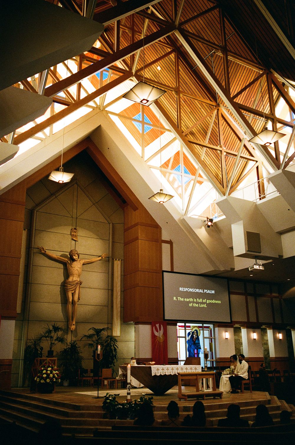Catholic church interior with large crucifix, wooden vaulted ceiling, and responsorial psalm displayed on screen during mass.