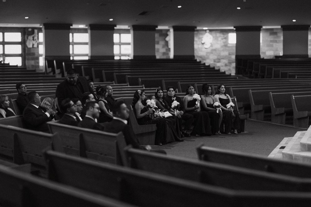Black and white photo of wedding party seated in church pews during ceremony.