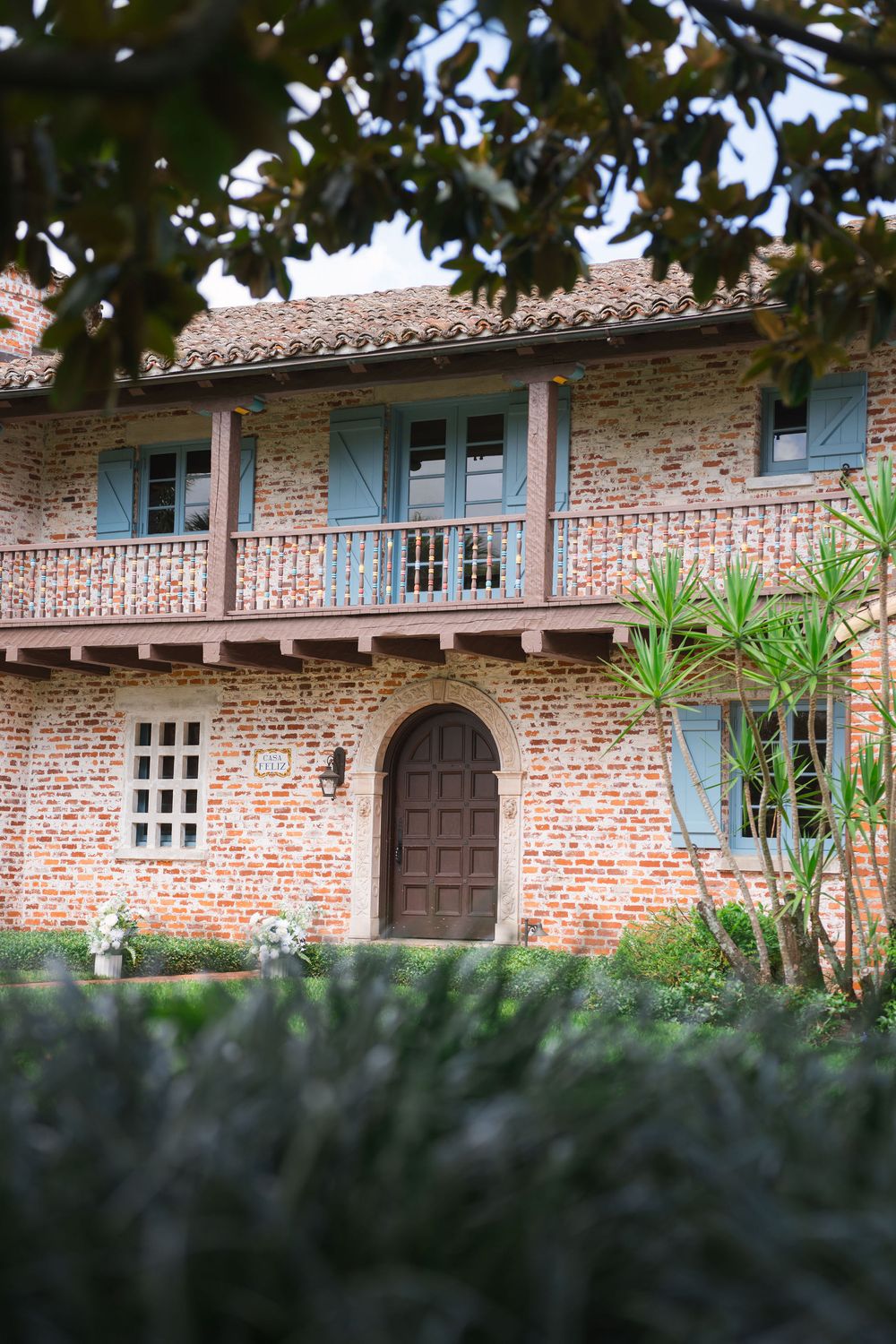 Historic Spanish colonial brick building with blue shutters and wooden doors surrounded by lush tropical foliage.