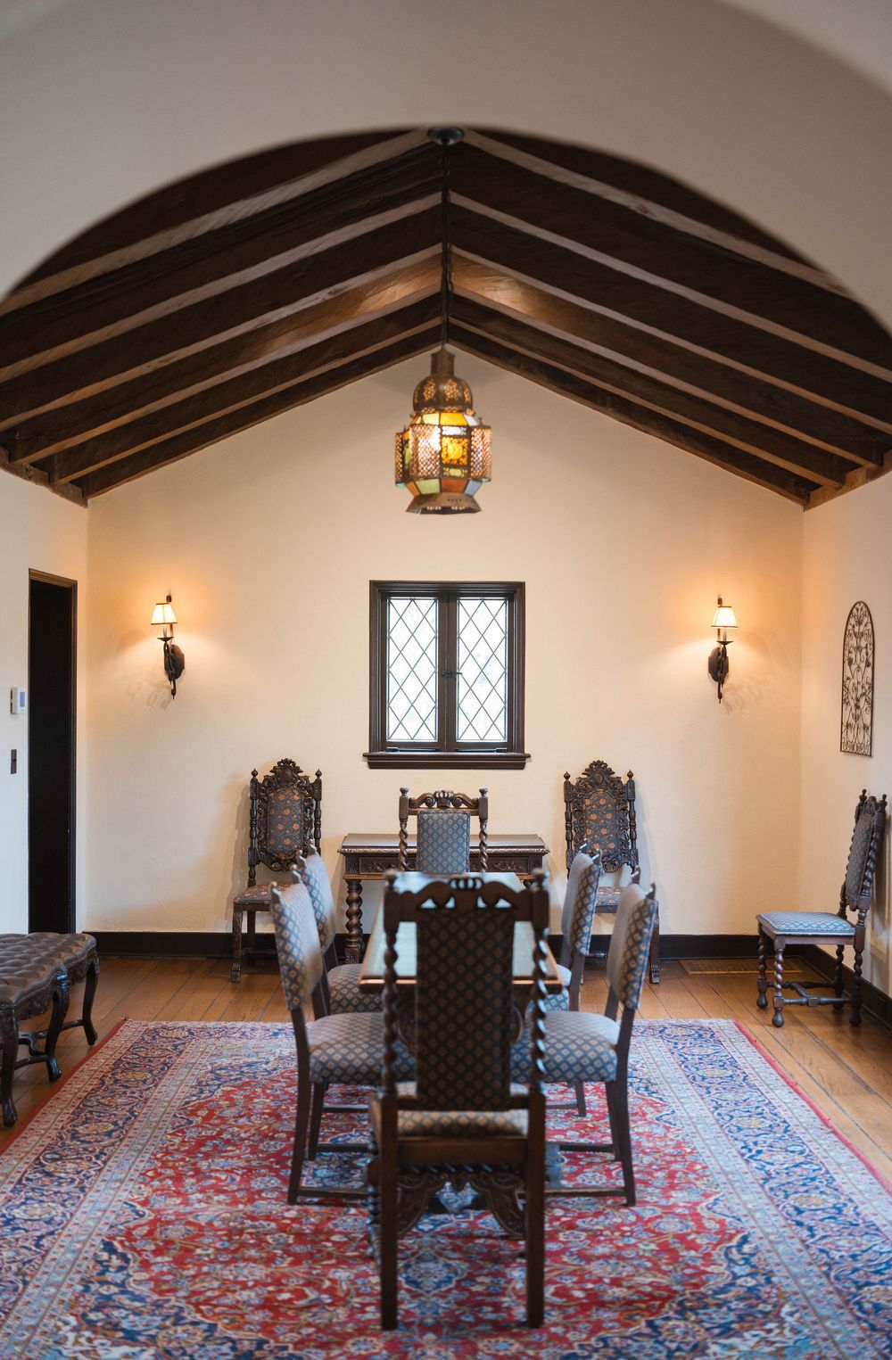 Interior room with dark wooden beams, antique chairs, and red patterned rug in historic medieval castle great hall.