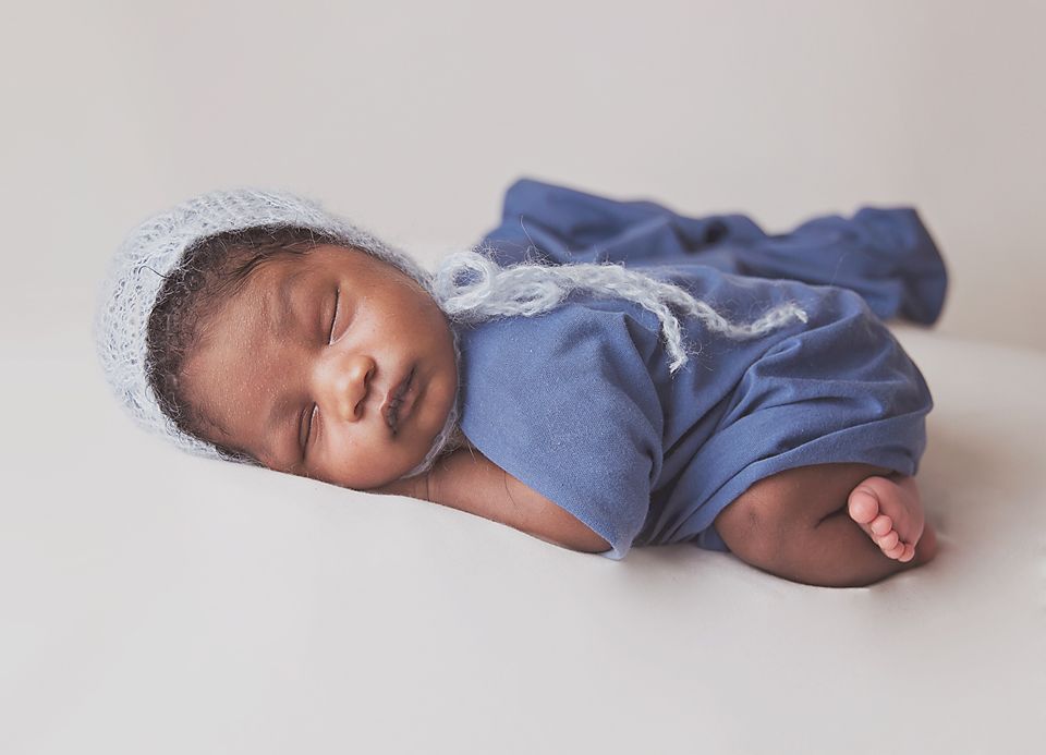 A sleeping baby in a blue onesie lying on a white surface in a series of connected photos.