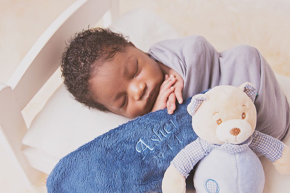 Baby in blue onesie sleeping peacefully on white bedding with a pacifier.