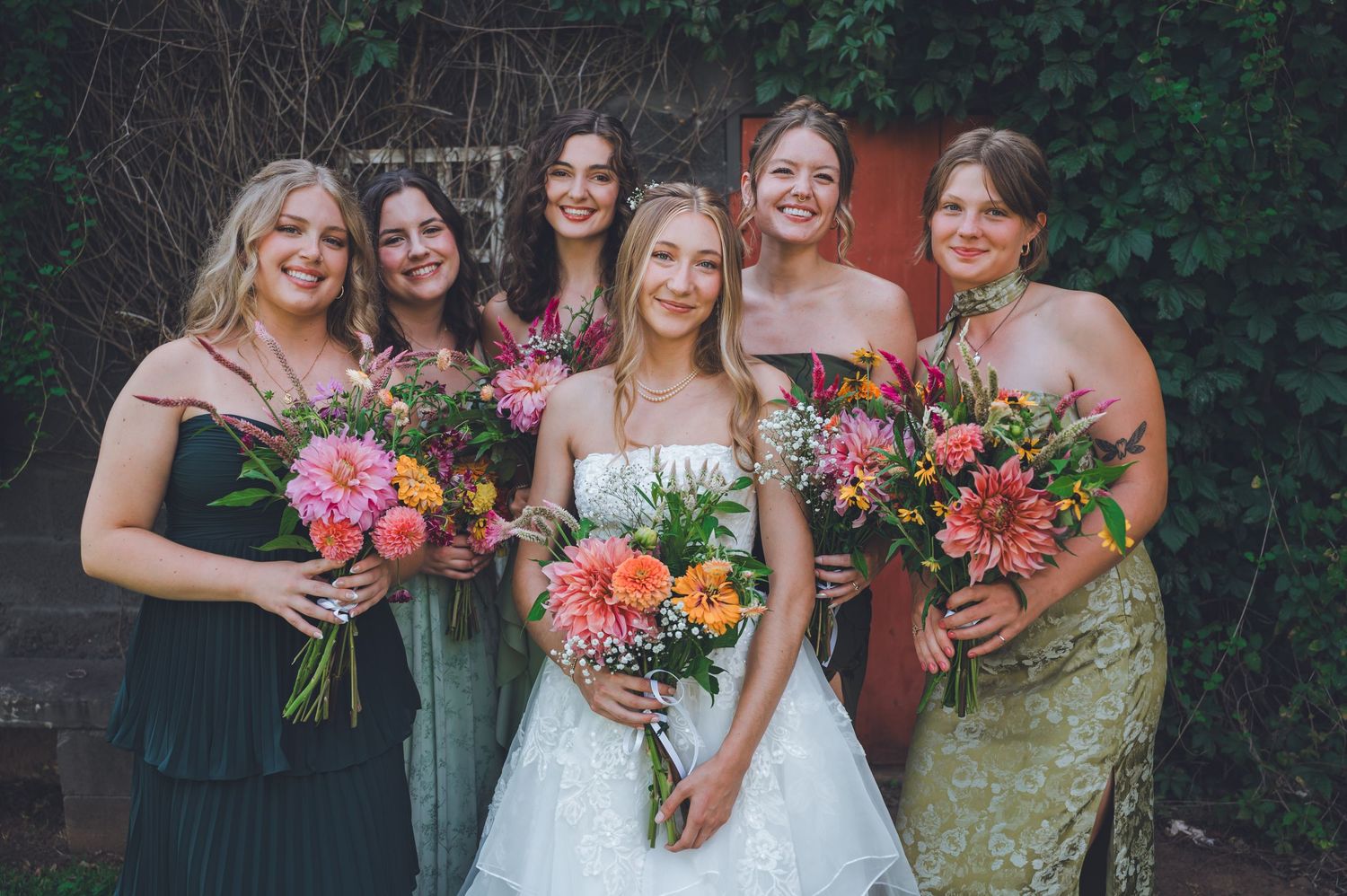 A wedding party holds vibrant coral and pink bouquets while posing together outdoors.