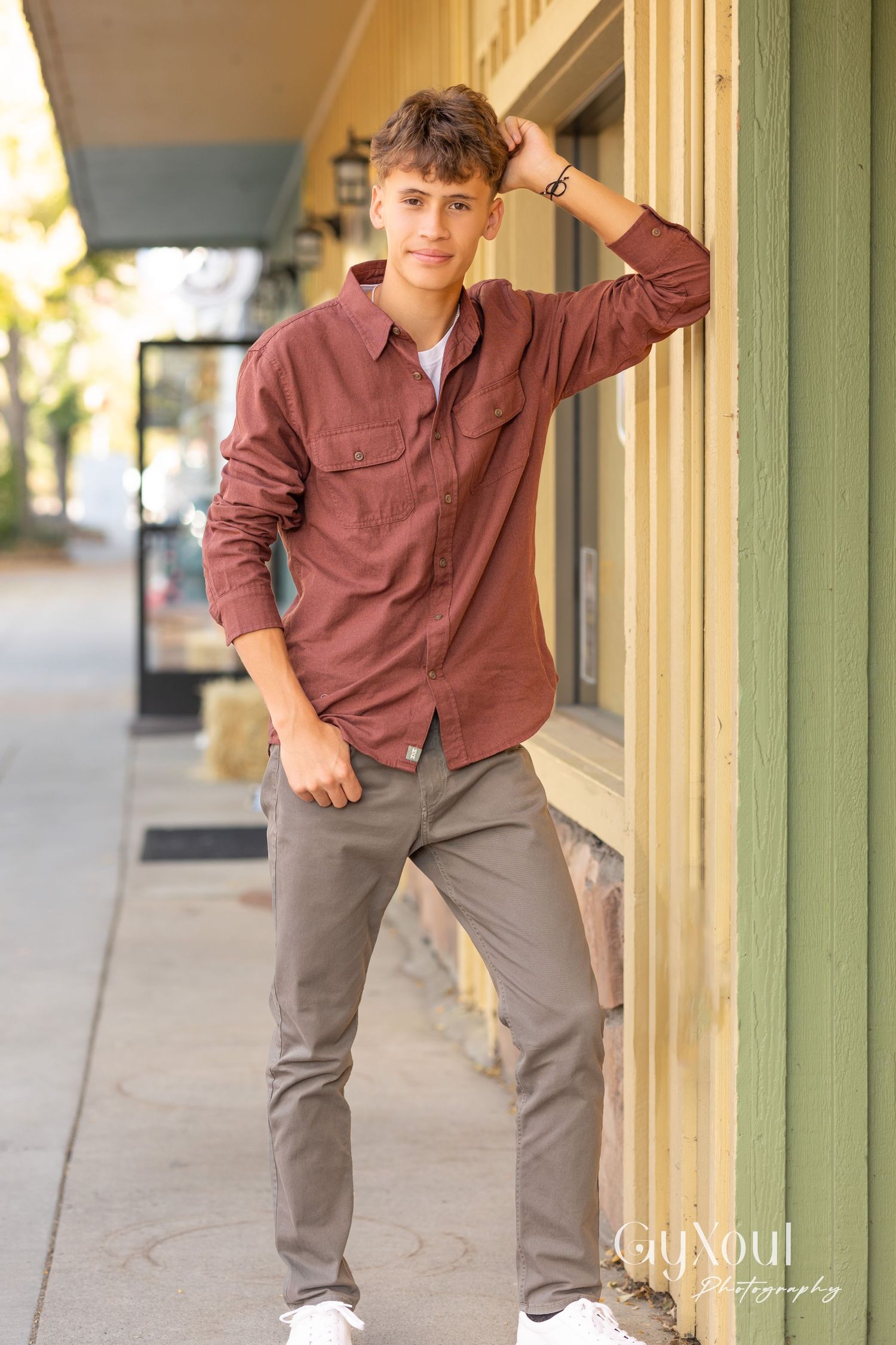 Casual street style photo of person in burgundy button-up shirt leaning against yellow building.