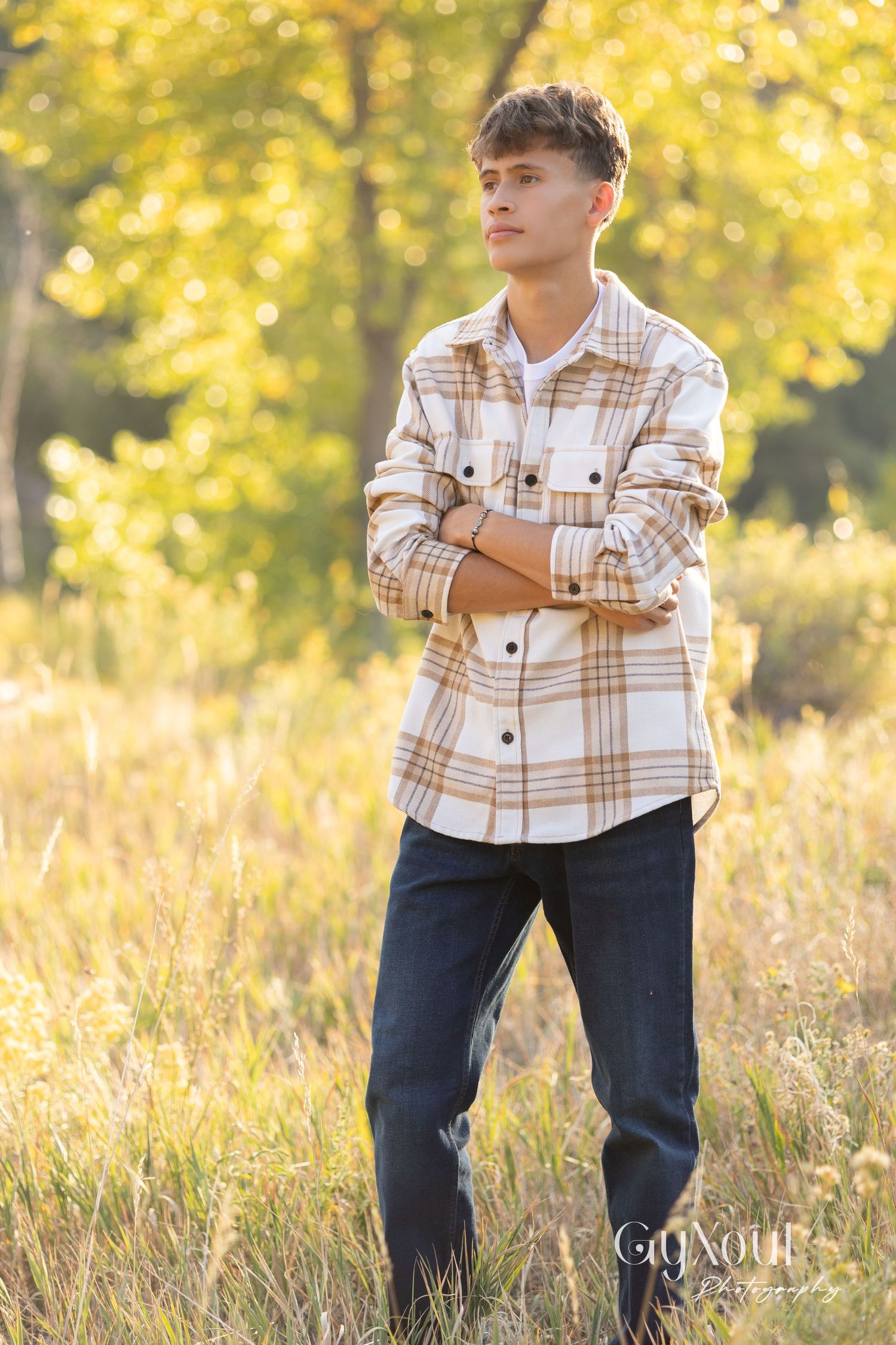 Person in plaid shirt and jeans stands in tall grass during golden hour.