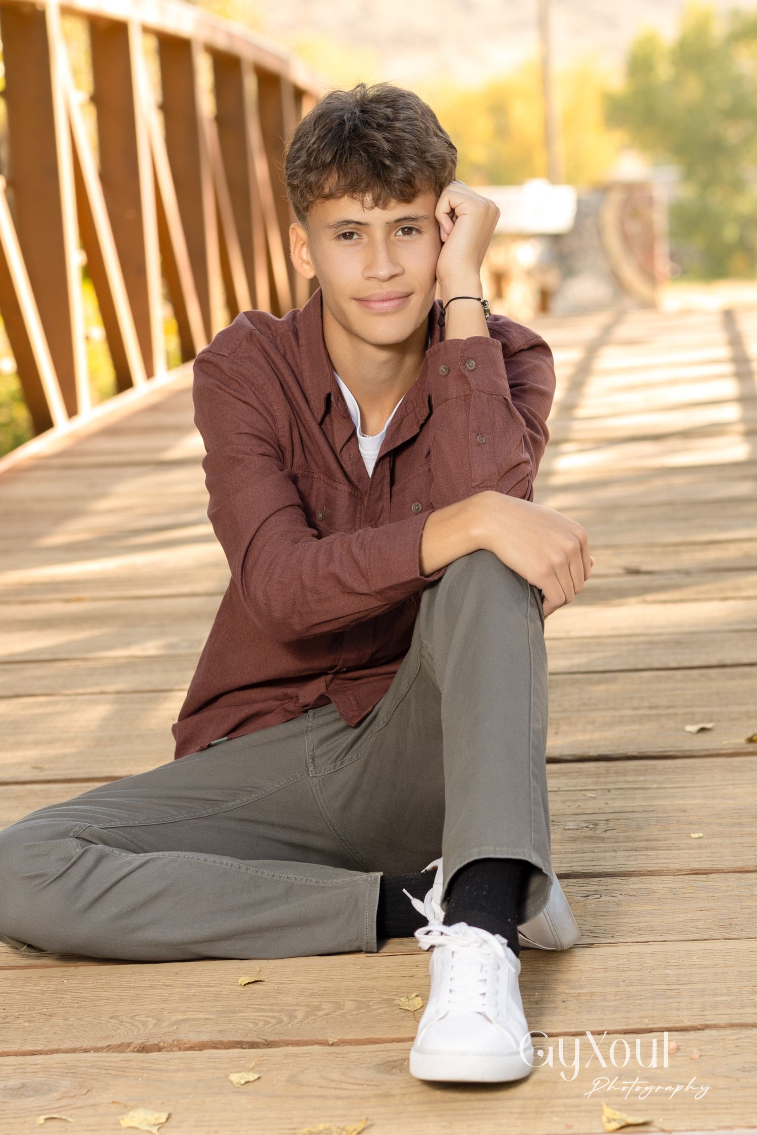 Student poses casually on wooden bridge wearing burgundy jacket and gray pants.