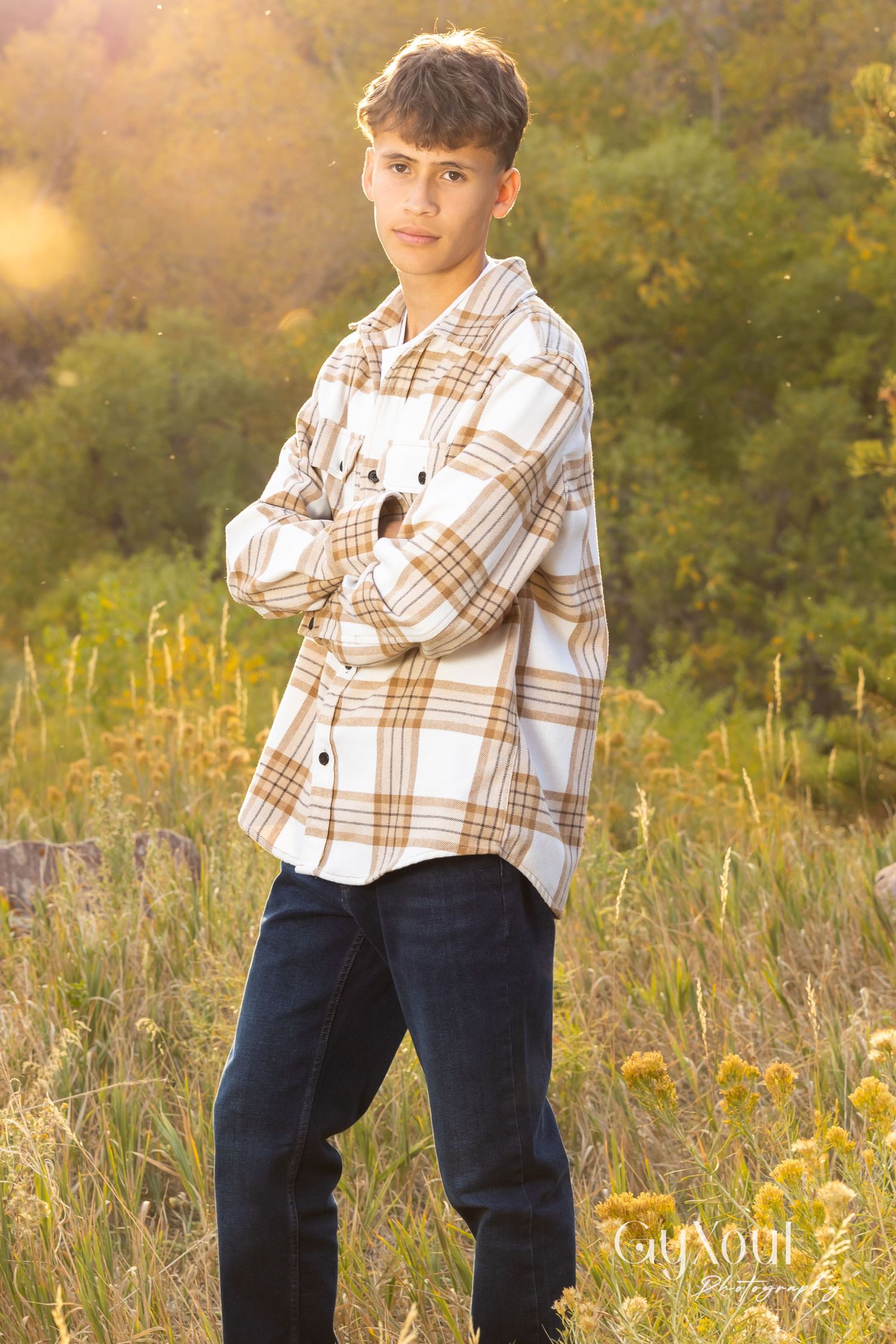 Portrait of young person in plaid flannel shirt against golden sunset background.
